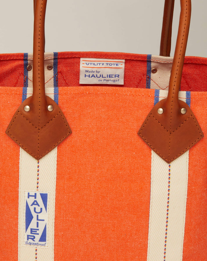 Close-up image of small classic canvas tote bag in orange colour with tan leather handles and contrasting stripes and HAULIER branding.