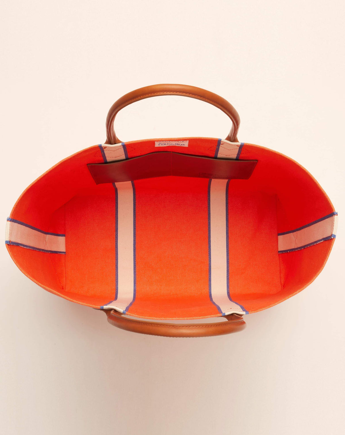 Image of inside of classic canvas tote bag in bright orange colour with tan leather handles and contrasting natural ecru stripes.