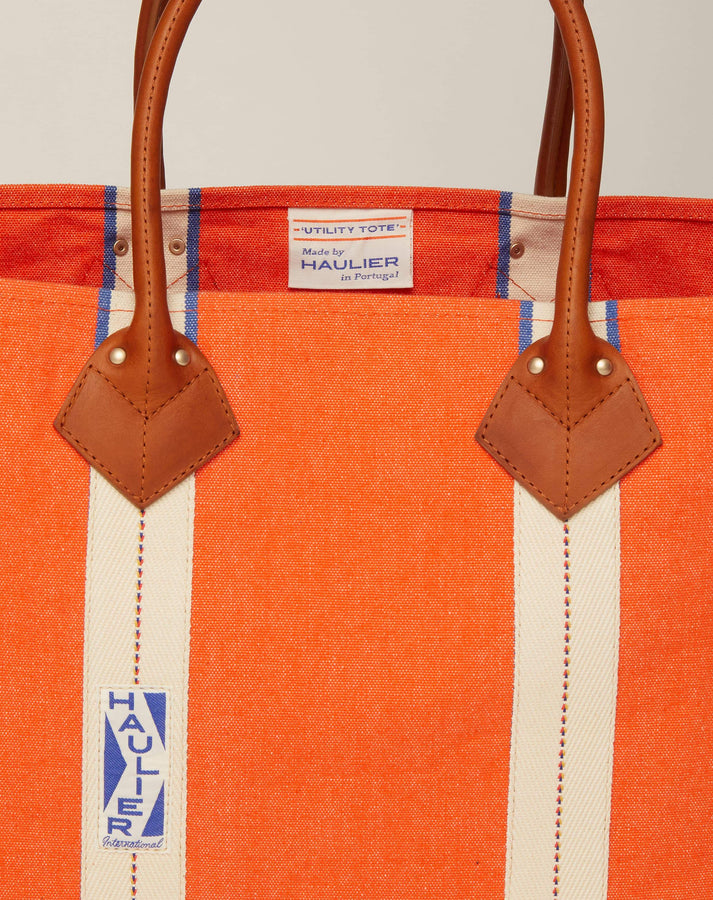 Close-up image of medium-sized classic canvas tote bag in orange colour with tan leather handles and contrasting stripes and HAULIER branding.