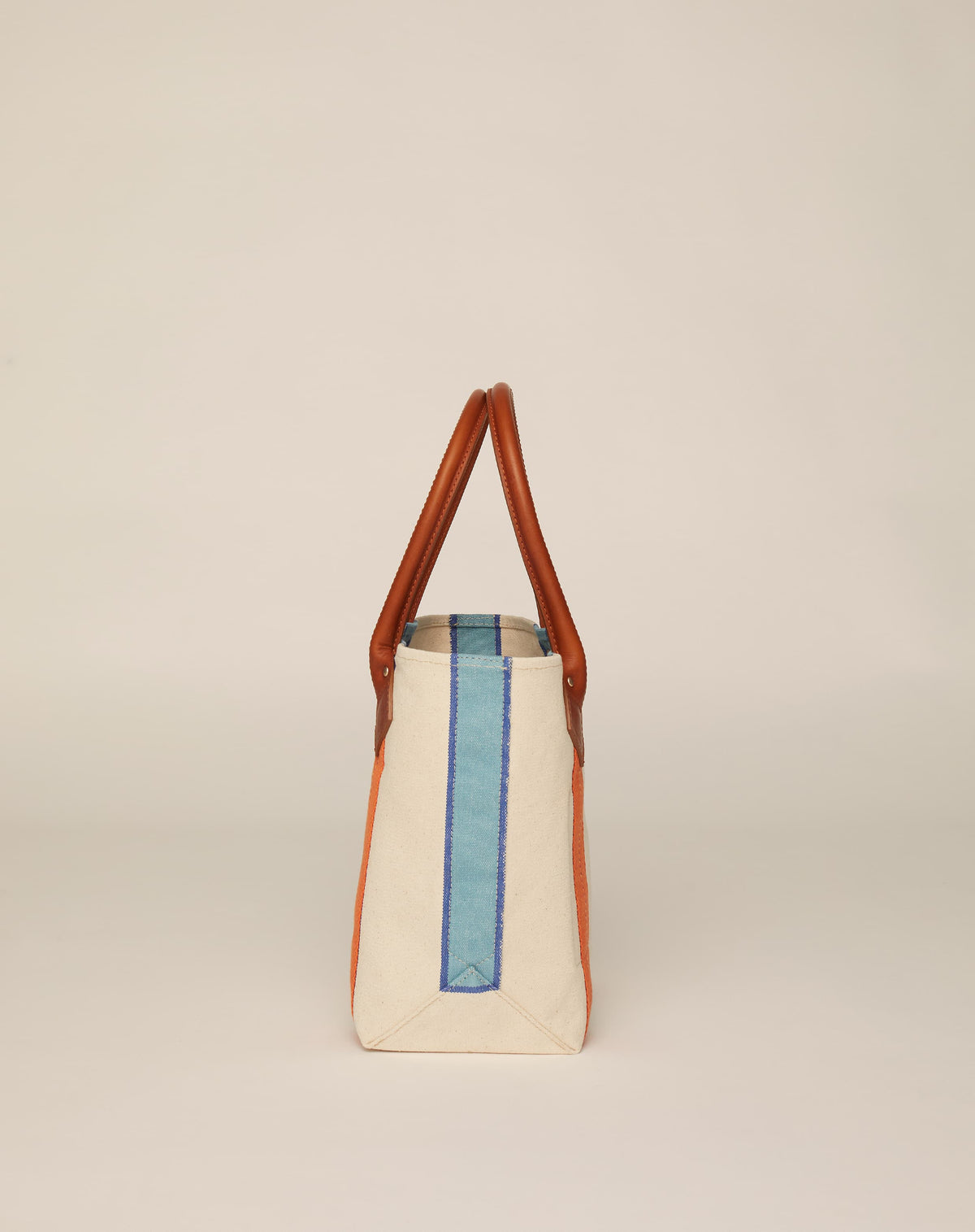 Side image of small classic canvas tote bag in natural ecru colour with tan leather handles and contrasting stripes.