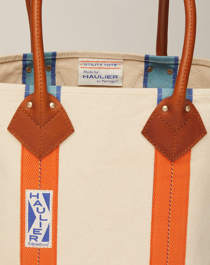 Close-up image of small classic canvas tote bag in natural ecru colour with tan leather handles and contrasting stripes and HAULIER branding.