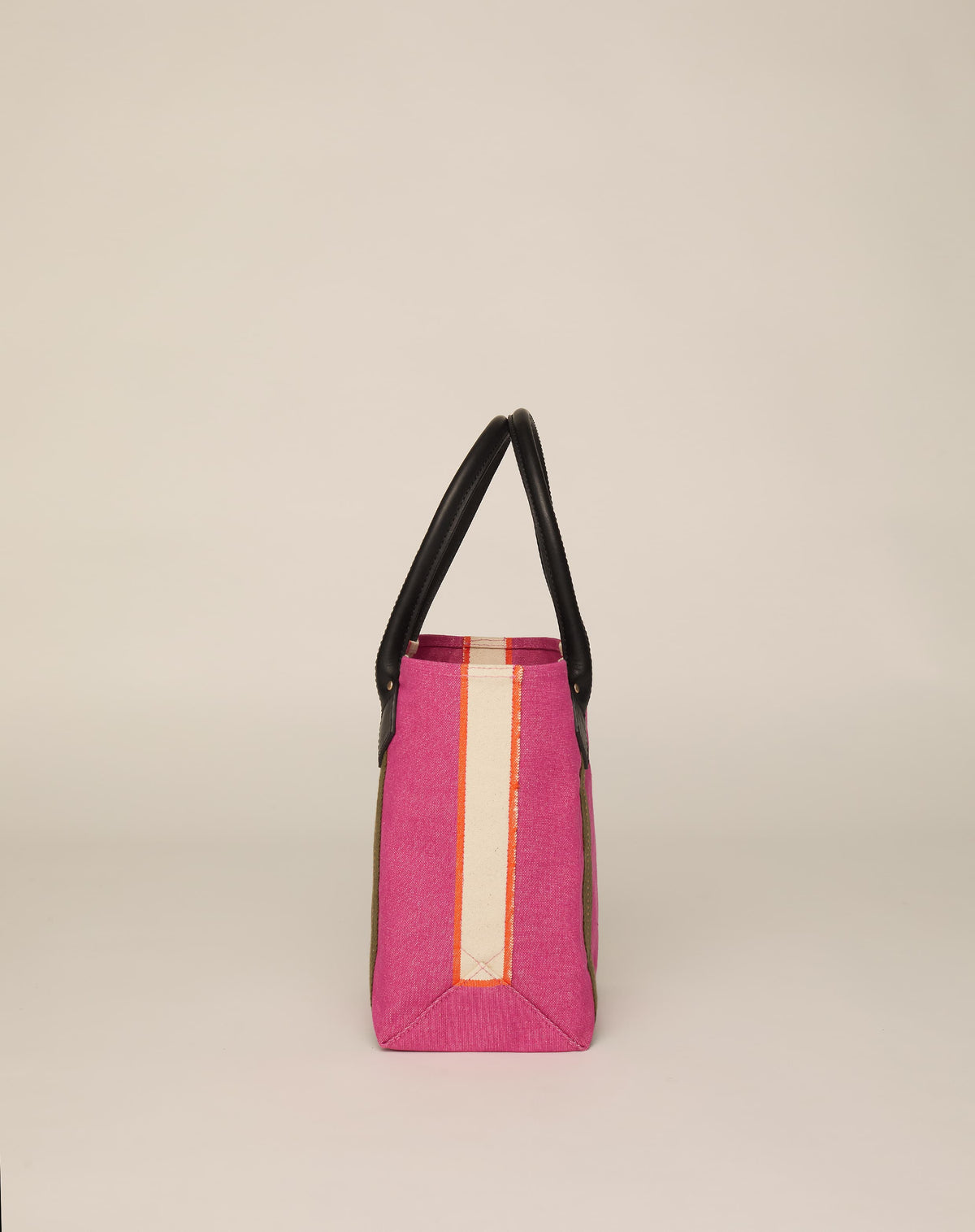 Side image of small classic canvas tote bag in fuchsia colour with black leather handles and contrasting stripes.