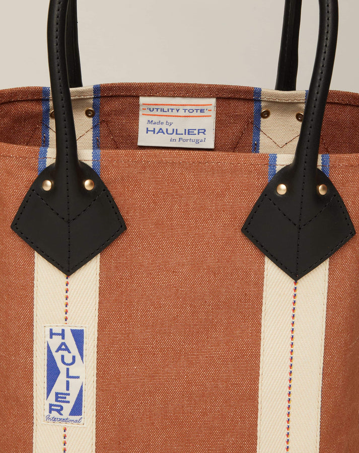 Close-up image of small classic canvas tote bag in tan colour with black leather handles and contrasting stripes and HAULIER branding.