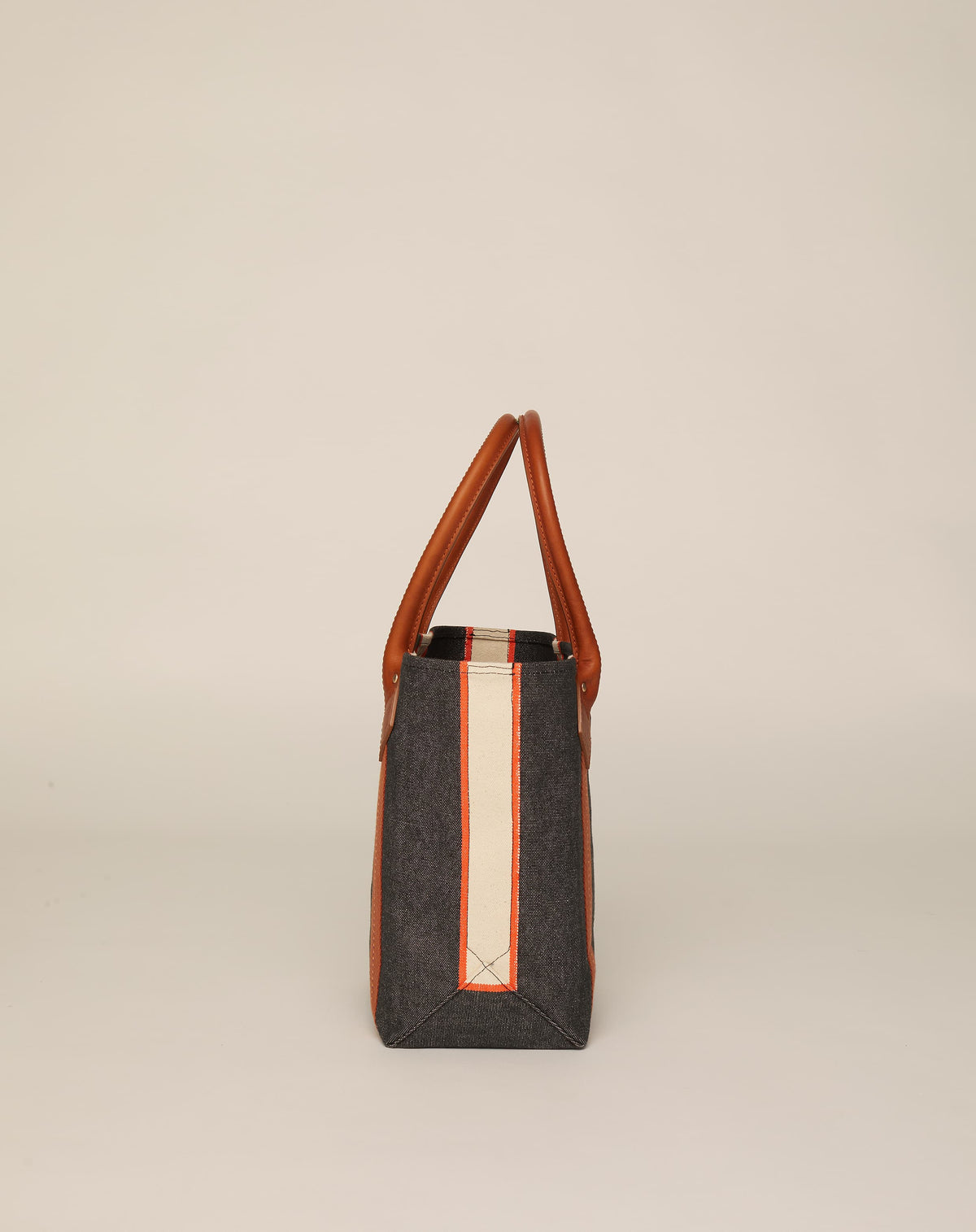 Side image of small classic canvas tote bag in washed black colour with tan leather handles and contrasting stripes.