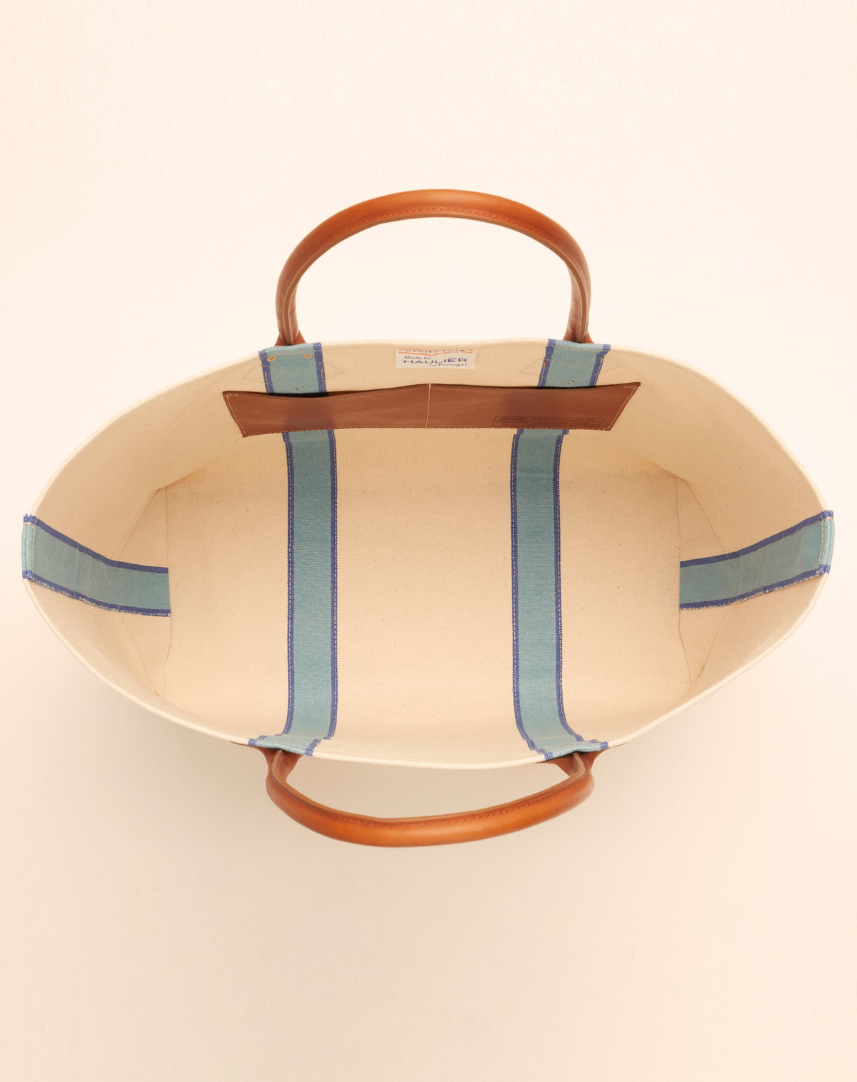 Image of inside of a classic canvas tote bag in natural ecru colour with leather handles and contrasting light blue stripes inside.